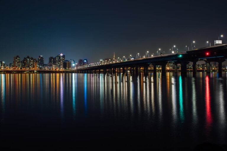 Stunning nighttime view of a city skyline and illuminated bridge reflections over water.