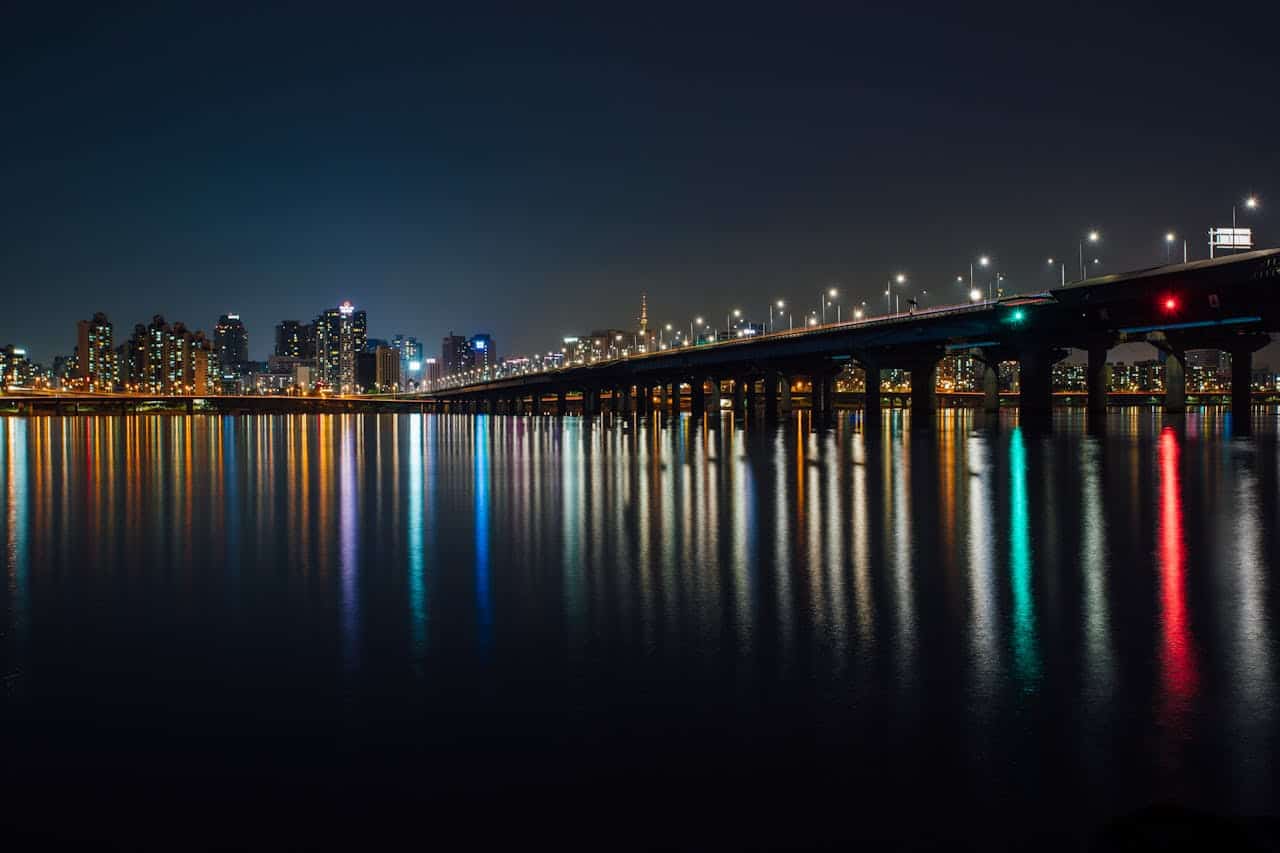 Stunning nighttime view of a city skyline and illuminated bridge reflections over water.